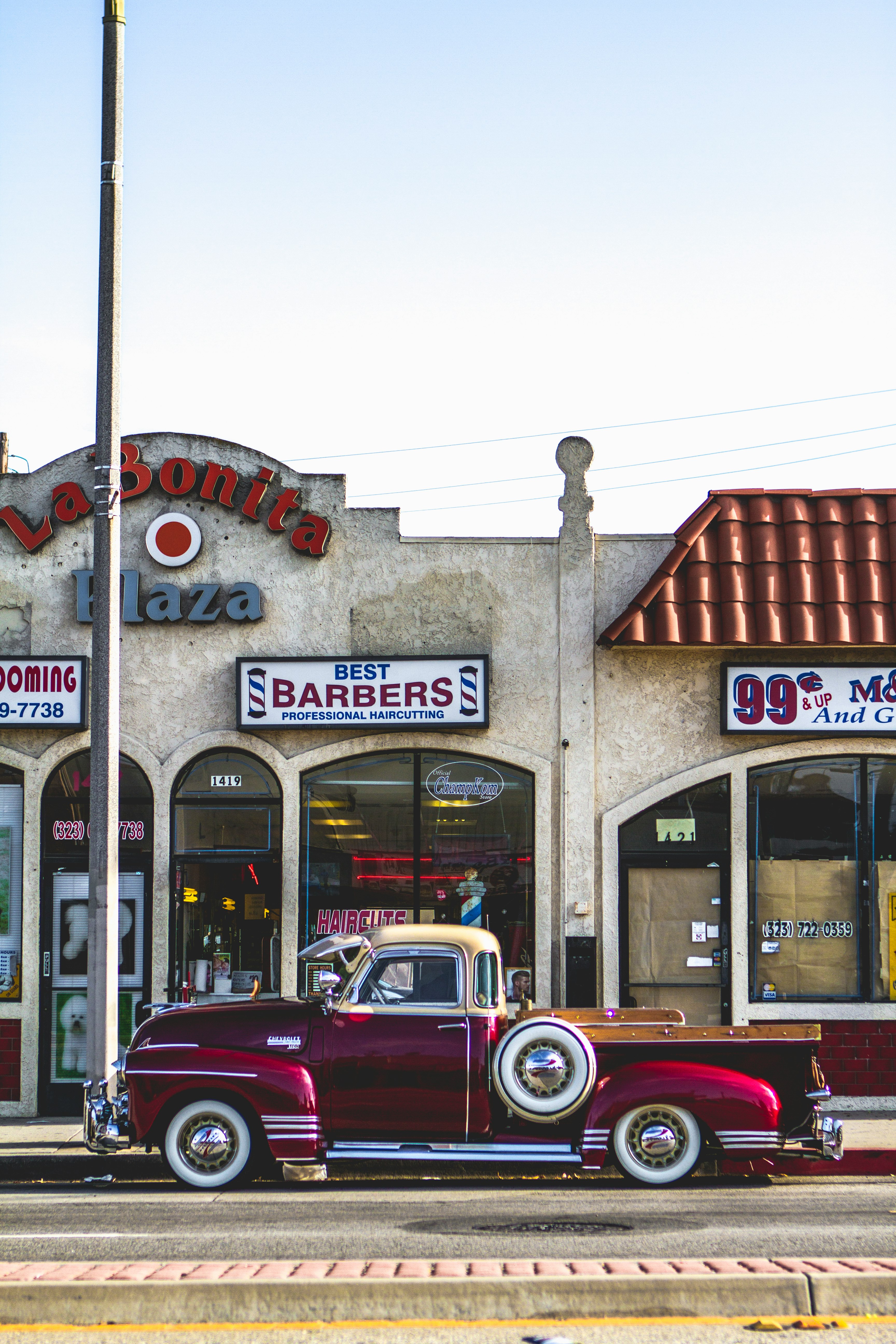 classic red coupe parked beside barber store facade